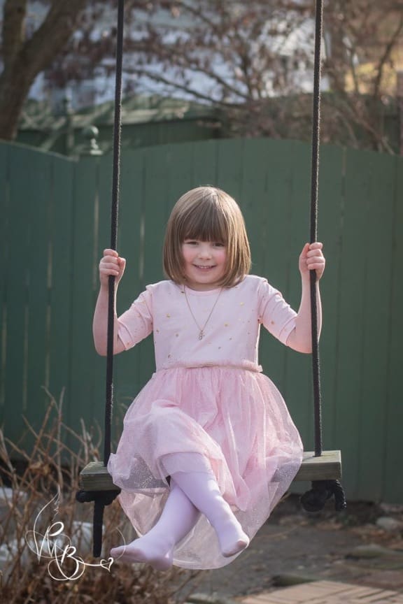 5 year old girl swings on tree swing in pink dress and tights